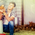 Cheerful male farmer holding brown chicken