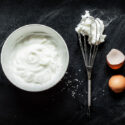whipped egg whites in bowl with whisk and egg shell
