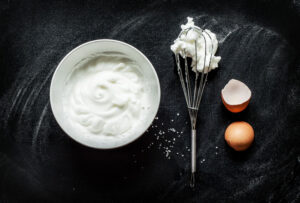 whipped egg whites in bowl with whisk and egg shell