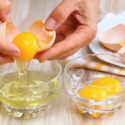 Woman hands breaking an egg to separate egg- white and yolks and egg shells at the background