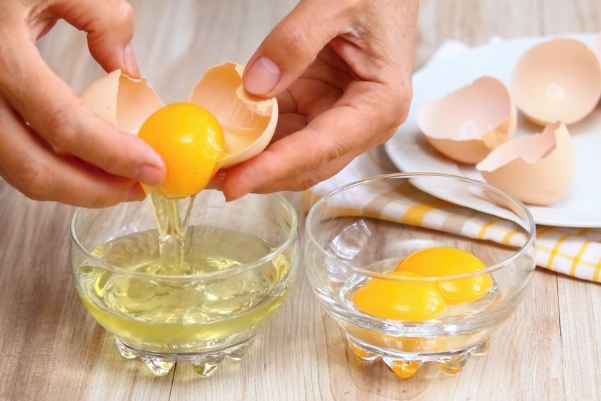 Woman hands breaking an egg to separate egg- white and yolks and egg shells at the background