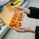 Woman chooses chicken eggs in a grocery store. Close up.