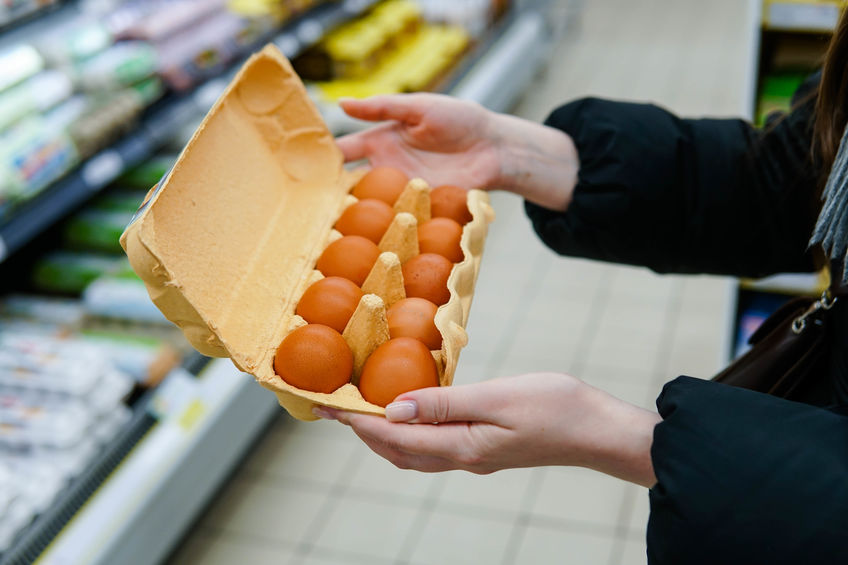 Woman chooses chicken eggs in a grocery store. Close up.