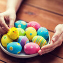 A woman reaching out toward a bowl containing decorated eggs.