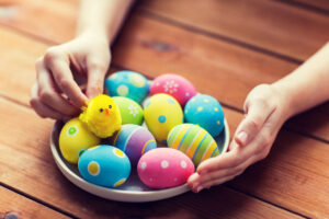 A woman reaching out toward a bowl containing decorated eggs.