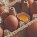 Fresh chicken eggs background. Brown and white eggs in craft carton pack on hay at rustic wood table, closeup. Rural still life, natural healthy food and organic farming concept.