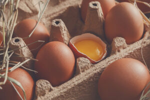 Fresh chicken eggs background. Brown and white eggs in craft carton pack on hay at rustic wood table, closeup. Rural still life, natural healthy food and organic farming concept.