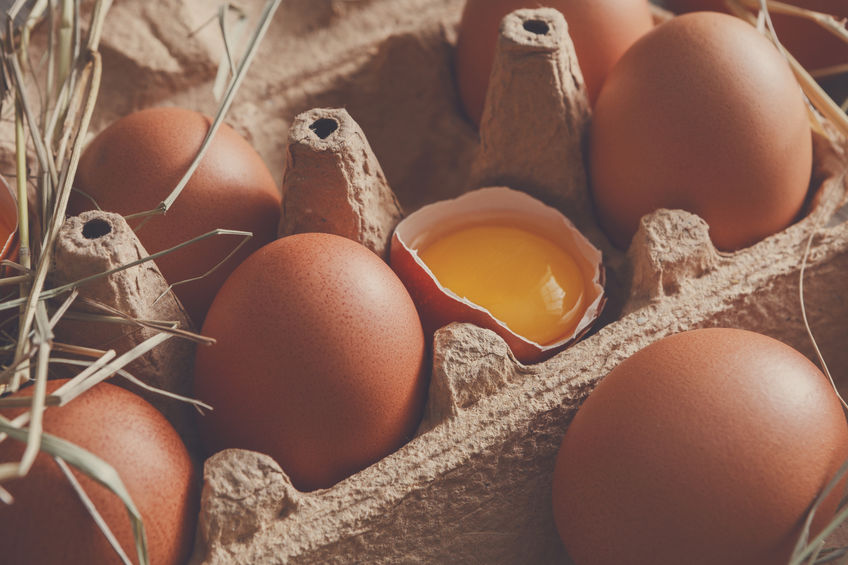 Fresh chicken eggs background. Brown and white eggs in craft carton pack on hay at rustic wood table, closeup. Rural still life, natural healthy food and organic farming concept.